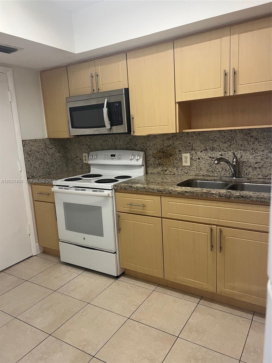 A kitchen features light wood cabinets, granite countertops, a white stove, and tile flooring — 16801 NE 14th Ave # 310, Miami FL 33162, MIAMI, FL