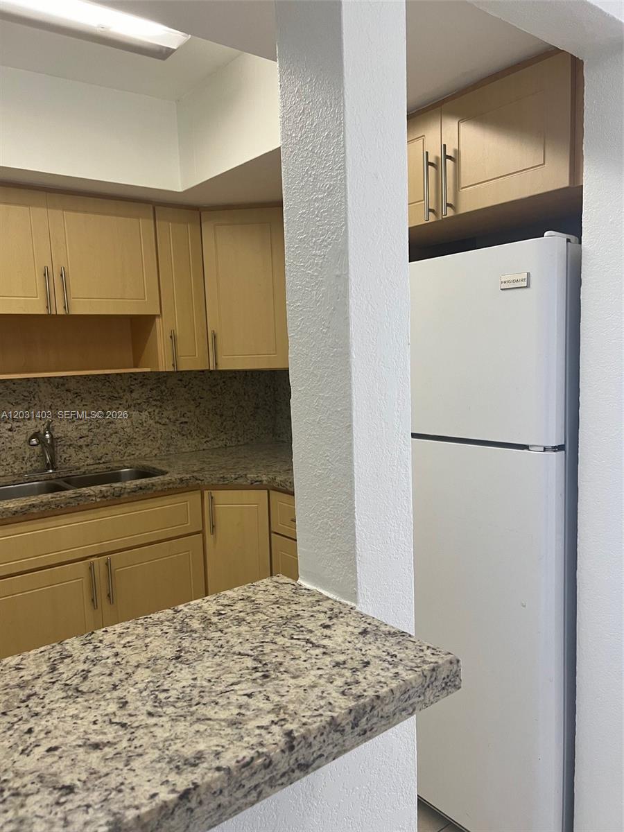 A kitchen features light wood cabinets, granite countertops, and a white top-freezer refrigerator — 16801 NE 14th Ave # 310, Miami FL 33162, MIAMI, FL