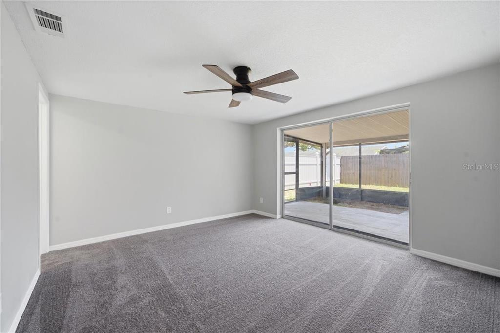 A carpeted bedroom features a ceiling fan, light gray walls, and sliding glass doors to a patio — 6224 KELLER DRIVE UNIT 2, PORT RICHEY, FL