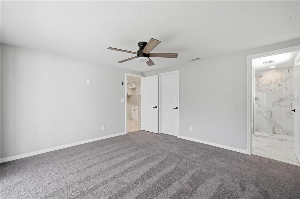 A bedroom with gray carpet, a ceiling fan, two white doors, and an attached bathroom — 6224 KELLER DRIVE UNIT 2, PORT RICHEY, FL