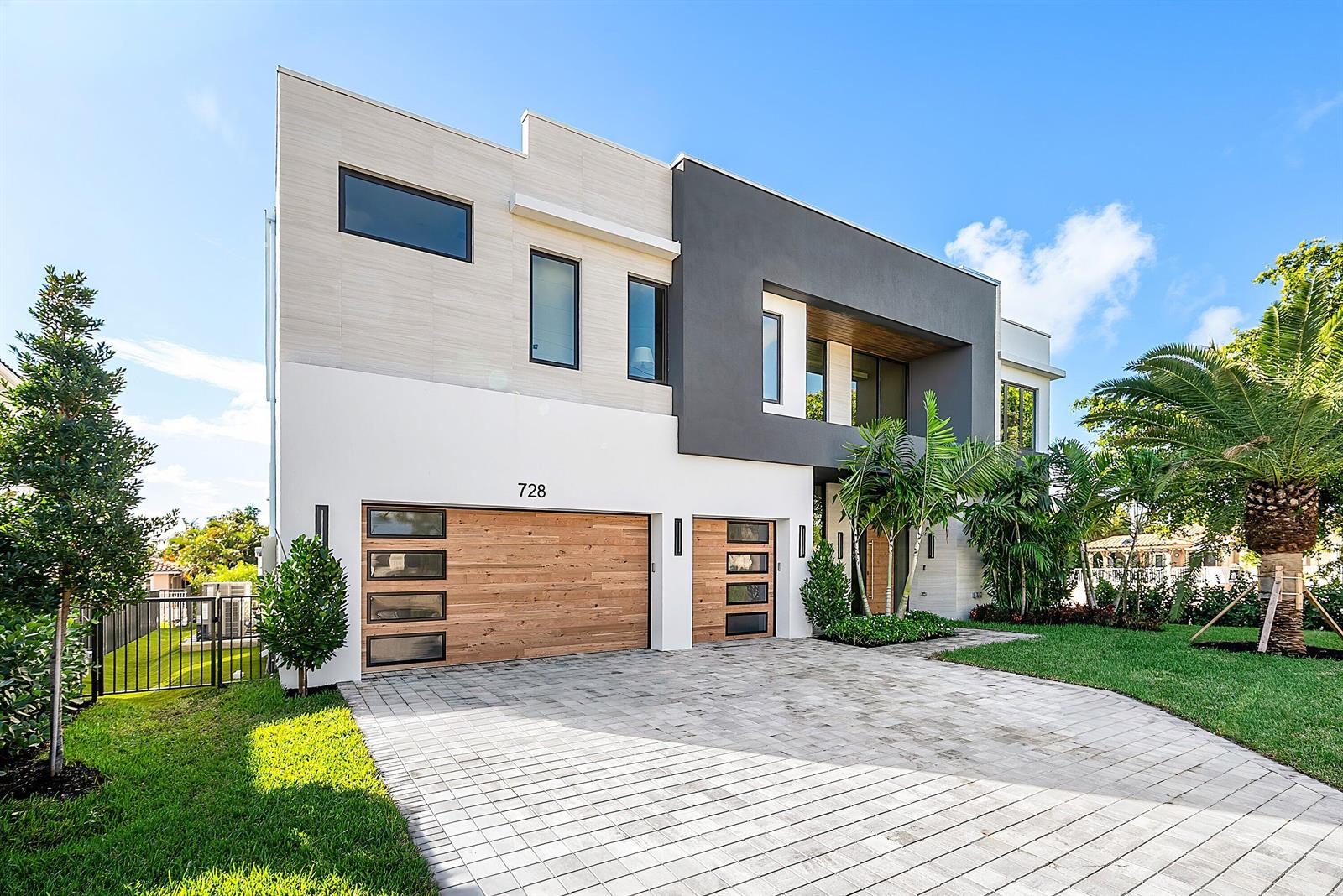 A modern two-story house features a paved driveway, wood-paneled garage doors, and palm trees — 728 Enfield Street, Boca Raton FL 33487, BOCA RATON, FL