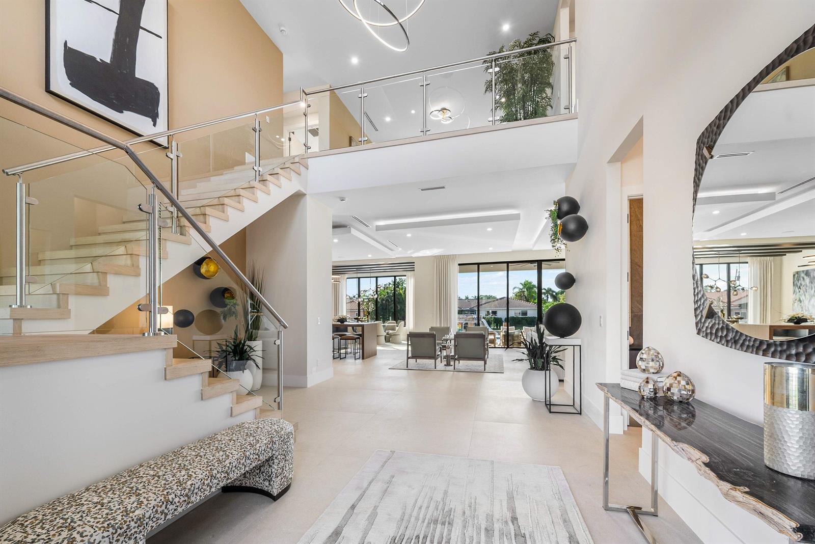 A modern, open-concept foyer features a glass-railed staircase, high ceilings, and a view toward the patio — 728 Enfield Street, Boca Raton FL 33487, BOCA RATON, FL