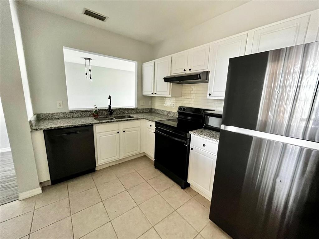 A kitchen features white cabinets, granite countertops, black appliances, and a tiled floor — 6011 SKYDALE WAY UNIT 201, RIVERVIEW, FL