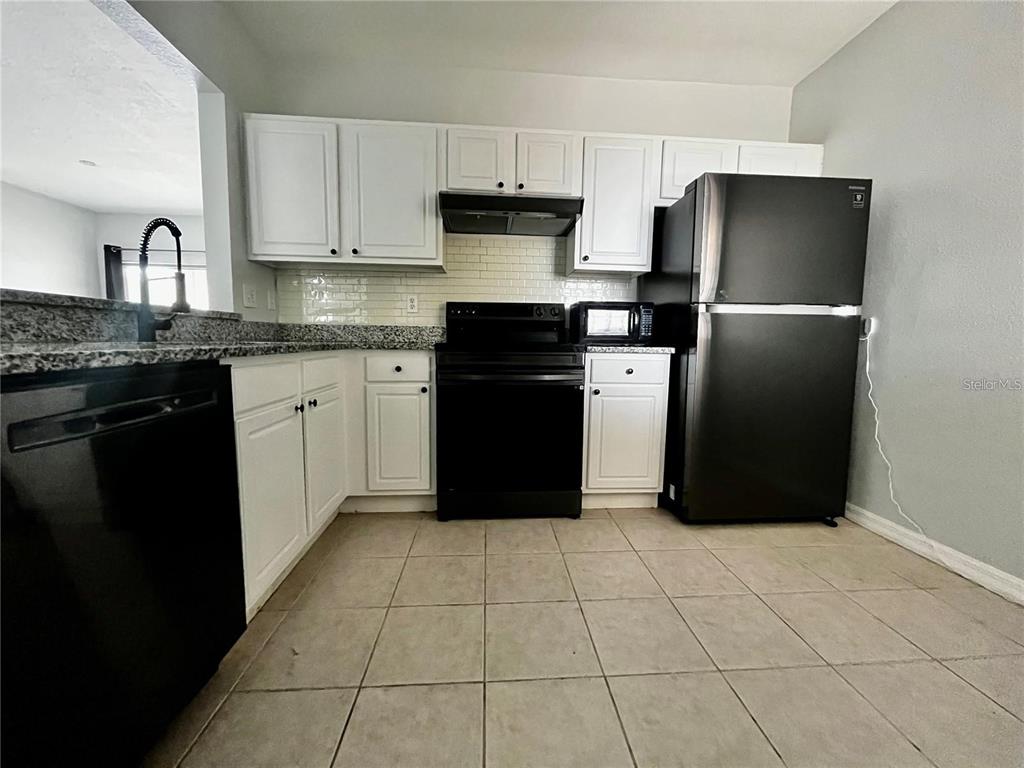 A kitchen features white cabinets, black appliances, granite countertops, and light-colored tile flooring — 6011 SKYDALE WAY UNIT 201, RIVERVIEW, FL