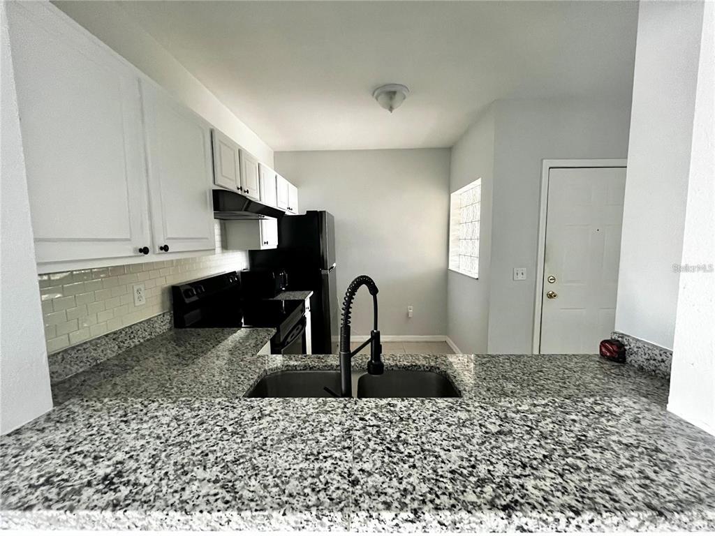 A kitchen features white cabinets, granite countertops, a double sink, and black appliances — 6011 SKYDALE WAY UNIT 201, RIVERVIEW, FL