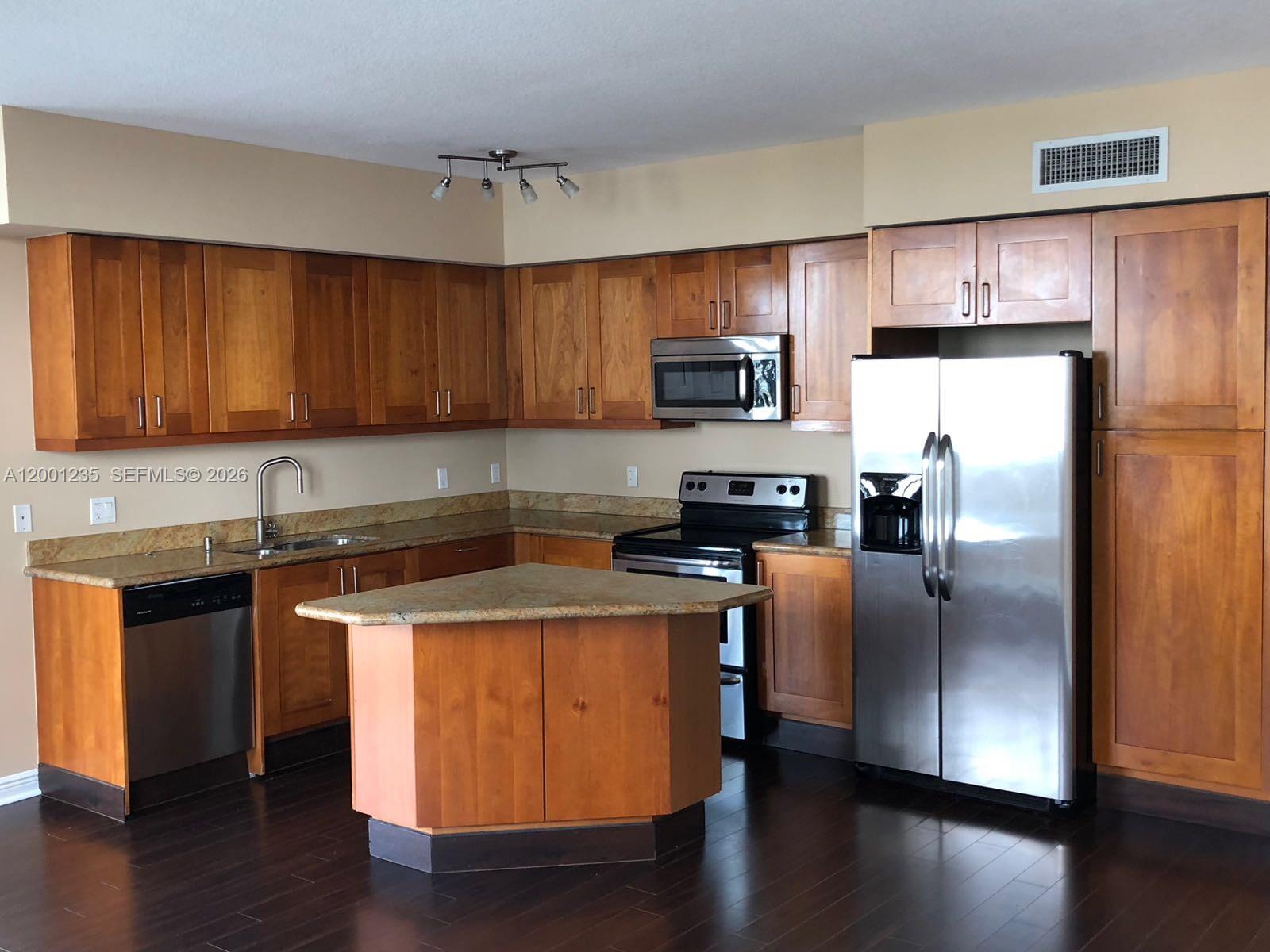 A kitchen features wood cabinets, stainless steel appliances, and a triangular island with stone countertops — 1755 E Hallandale Beach Blvd # 2002E, Hallandale Beach FL 33009, HALLANDALE BEACH, FL