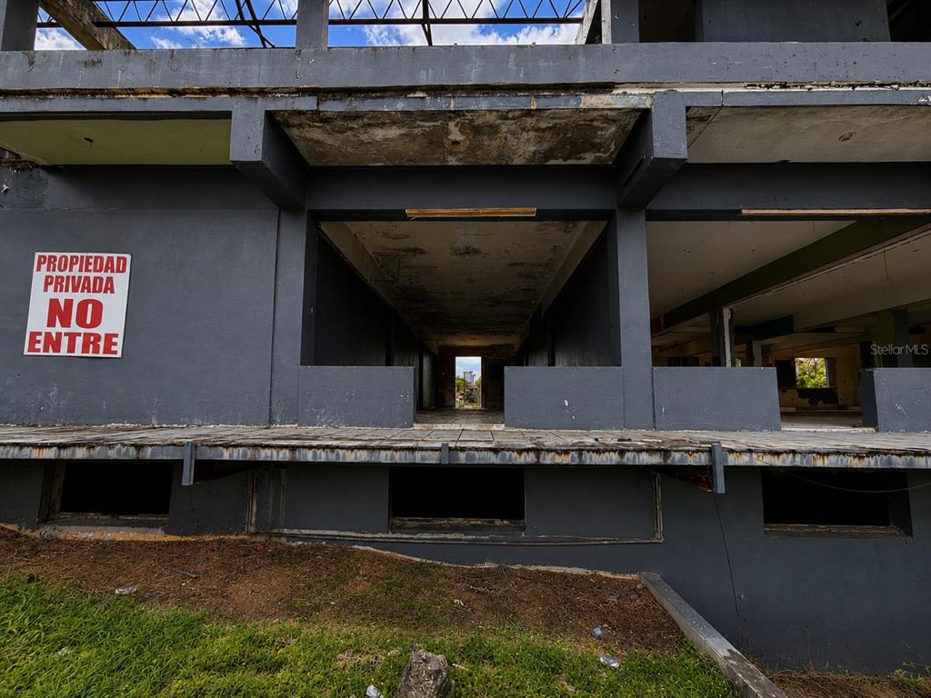 A view of the exterior of a dilapidated, unfinished concrete building with a warning sign — Calle 28 URB. MIRAFLORES, BAYAMON, PR