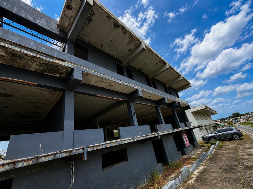 A low-angle exterior view of a multi-story, unfinished concrete building with open, wall-less levels — Calle 28 URB. MIRAFLORES, BAYAMON, PR