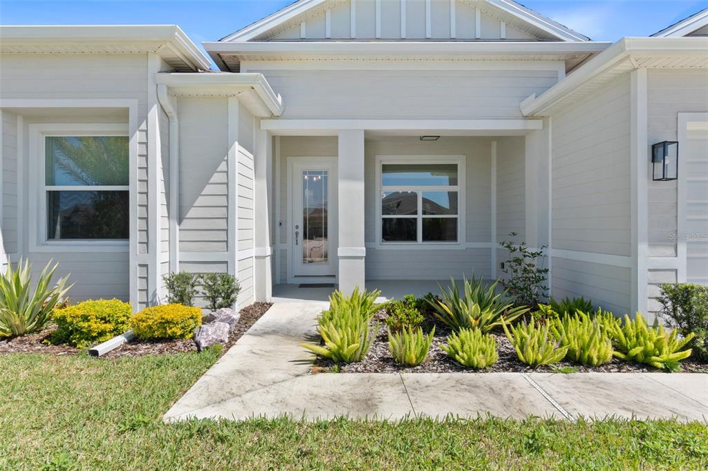 The exterior of a light-colored house features a covered entryway, a concrete walkway, and landscaping — 1329 TULLAMORE BOULEVARD, ORMOND BEACH, FL