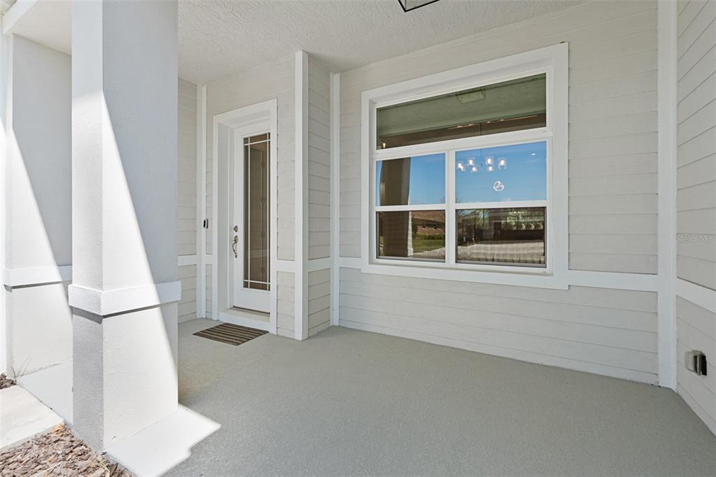 A covered front porch features light-colored horizontal siding, a glass-paneled door, and a large window — 1329 TULLAMORE BOULEVARD, ORMOND BEACH, FL
