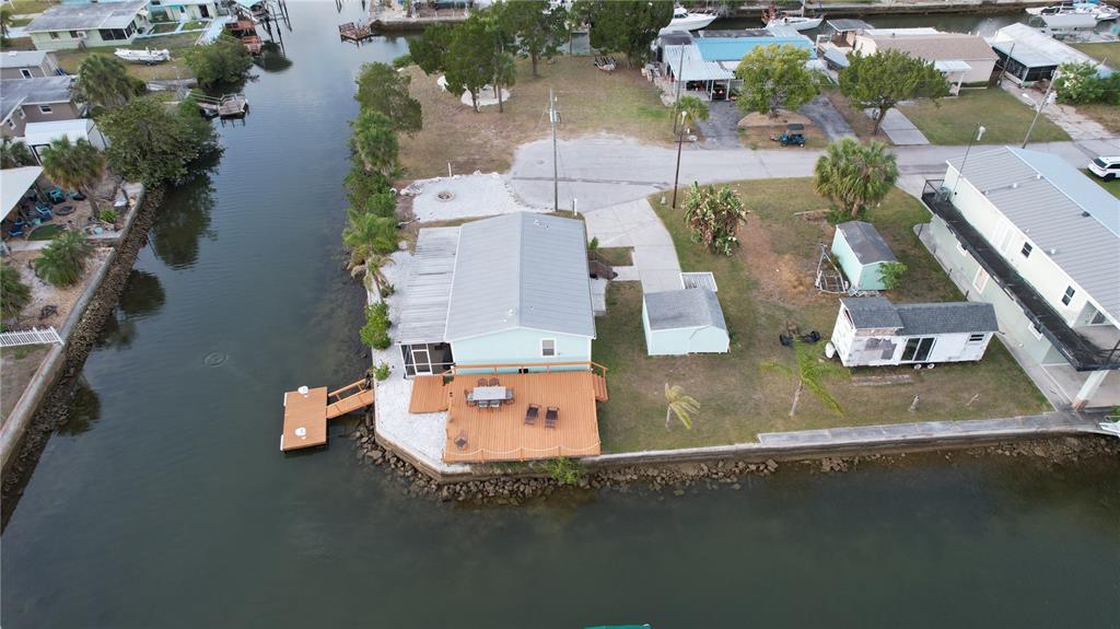 An aerial view shows a light-colored house with a wooden deck and dock on a canal — 6724 GULL LANE, HUDSON, FL