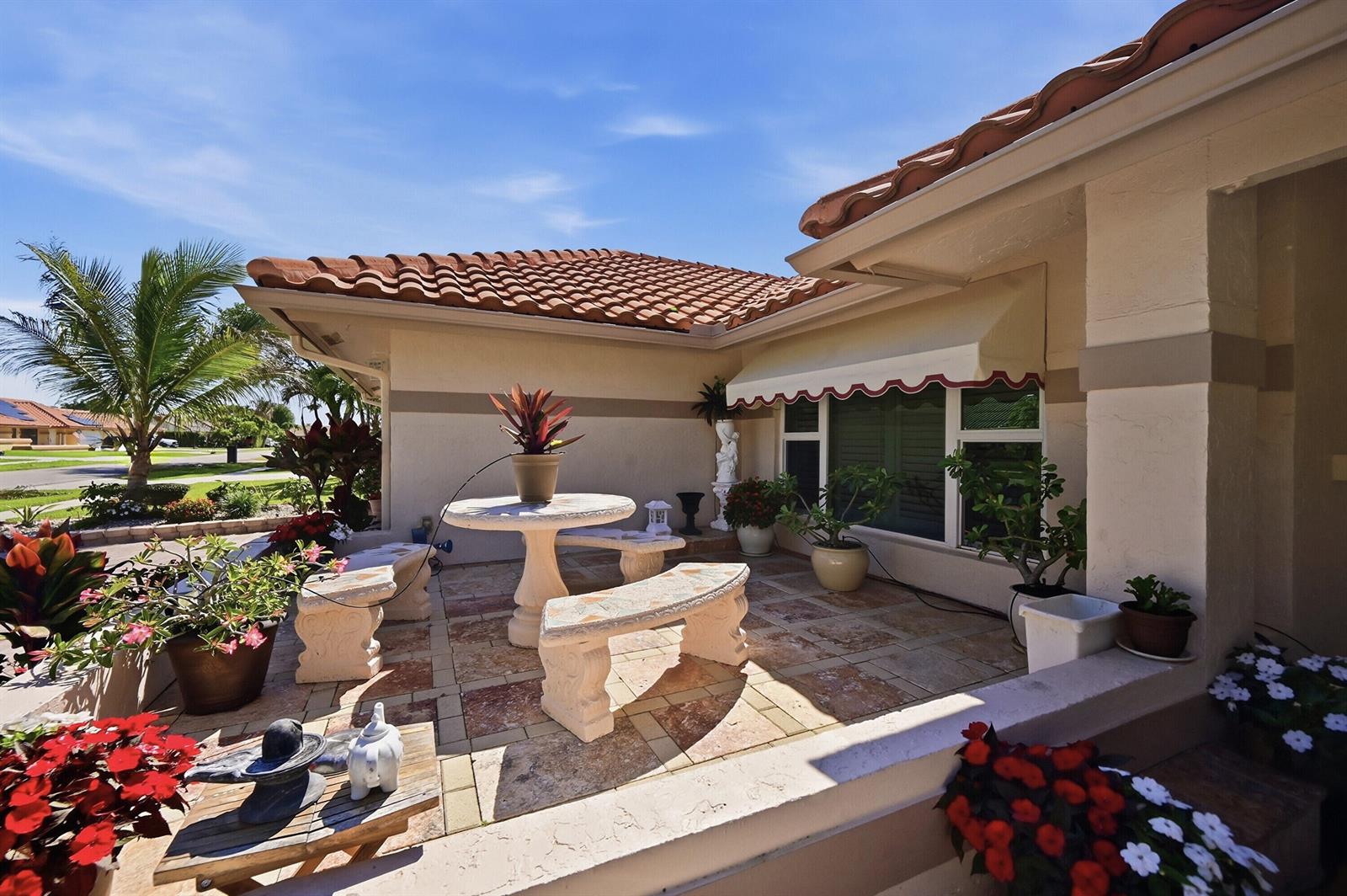 A patio with stone furniture, potted plants, and a red-tiled roof under a blue sky — 5884 Laurel Green Circle, Boynton Beach FL 33437, BOYNTON BEACH, FL