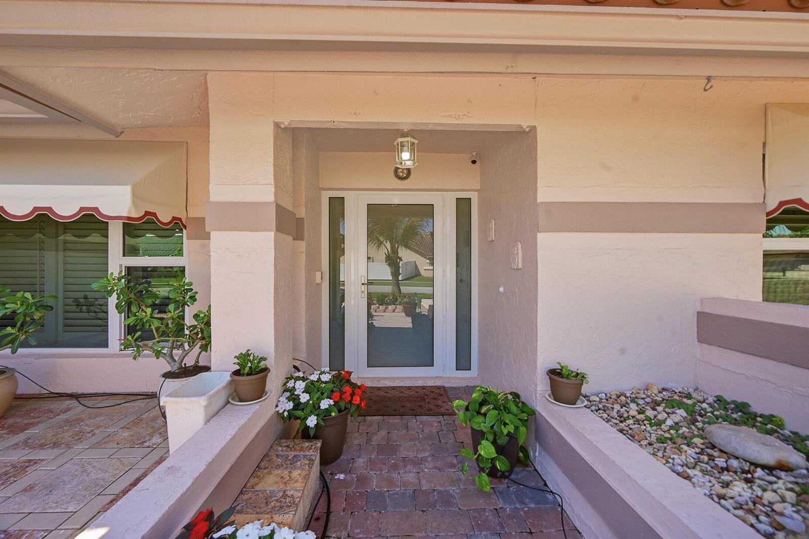 A front entryway with a glass door, potted plants, and a brick walkway — 5884 Laurel Green Circle, Boynton Beach FL 33437, BOYNTON BEACH, FL