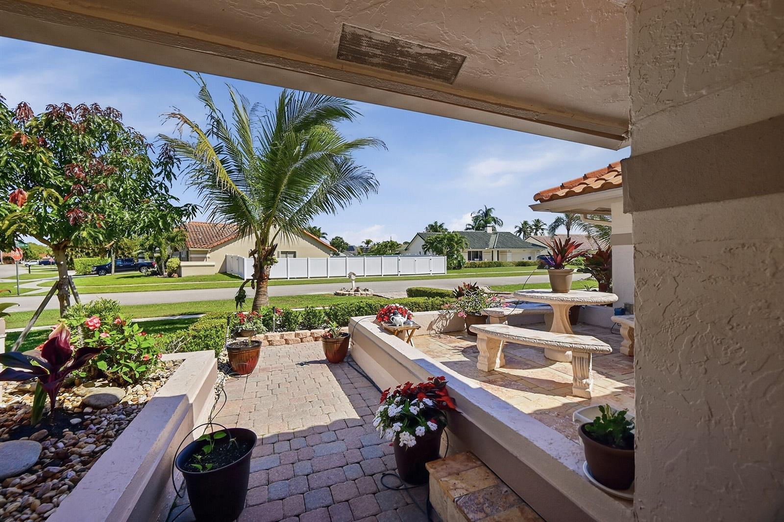 A paved patio with stone benches and potted plants overlooks a suburban street and lawn — 5884 Laurel Green Circle, Boynton Beach FL 33437, BOYNTON BEACH, FL