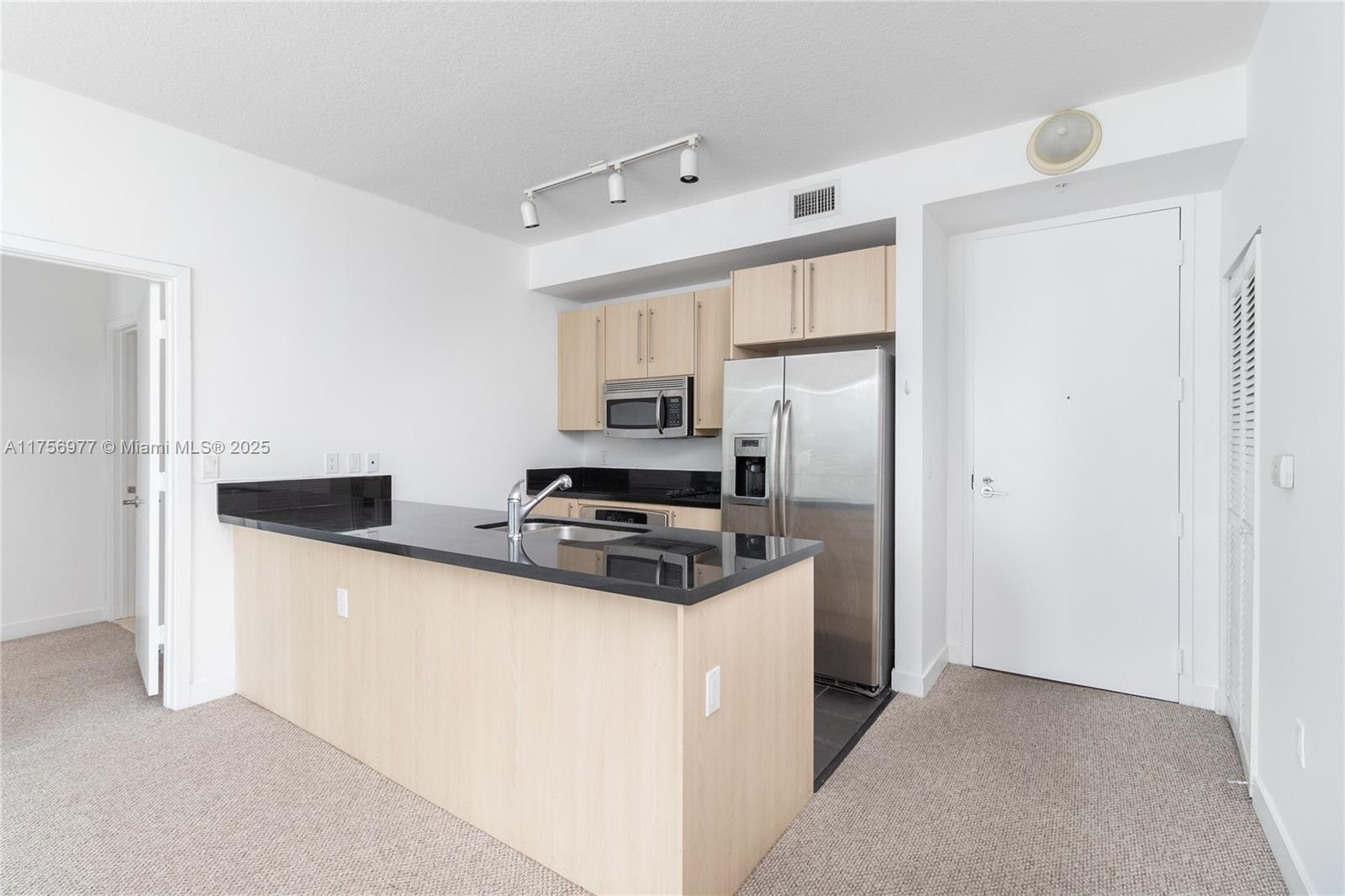 This kitchen features light wood cabinets, black countertops, stainless steel appliances, and carpeted flooring — 1111 SW 1st Ave, Miami FL 33130, MIAMI, FL