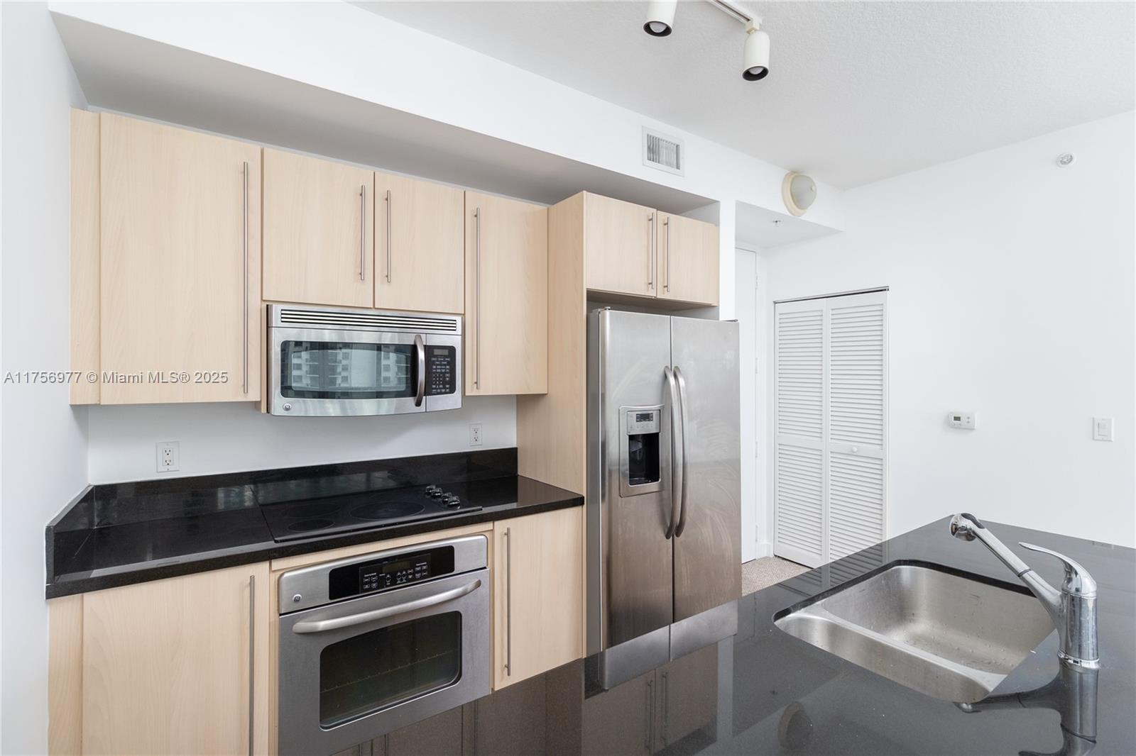 A kitchen features light wood cabinets, black countertops, stainless steel appliances, and a sink island — 1111 SW 1st Ave, Miami FL 33130, MIAMI, FL