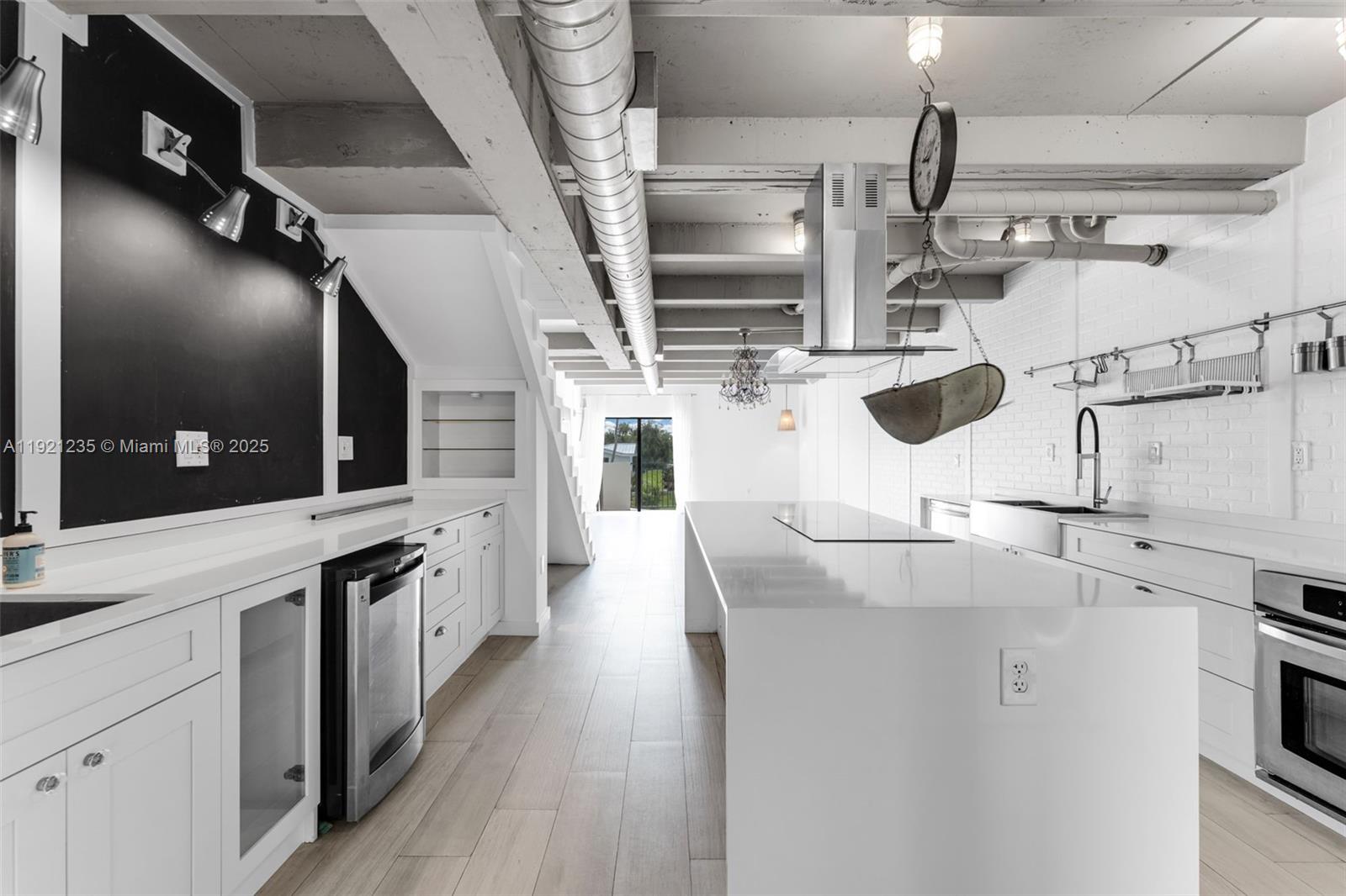 A modern kitchen features white cabinetry, a large island, exposed ductwork, and a chalkboard wall — 6901 Edgewater Dr # 315, Coral Gables FL 33133, CORAL GABLES, FL