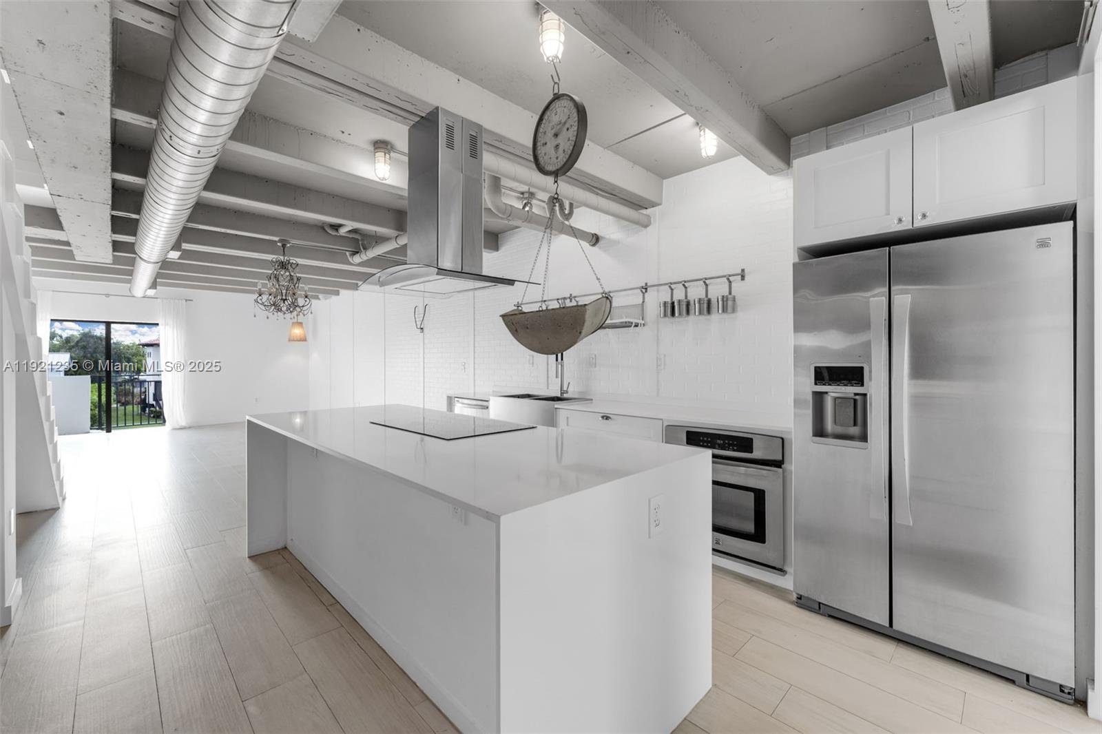 A modern kitchen features a white island, stainless steel appliances, and exposed ceiling beams — 6901 Edgewater Dr # 315, Coral Gables FL 33133, CORAL GABLES, FL