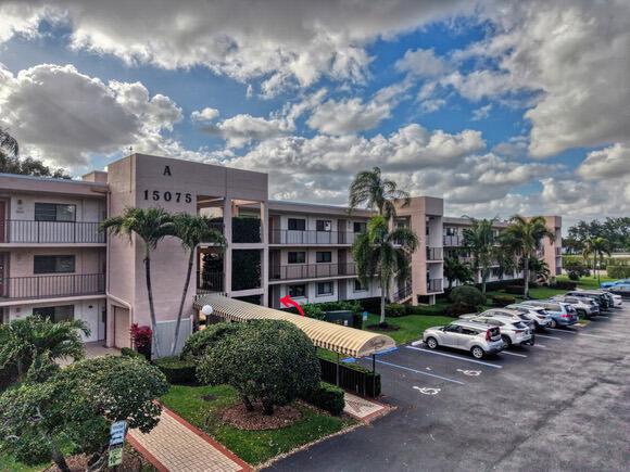 An aerial view shows a multi-story apartment building with a parking lot and pond — 15075 Witney Road # 108, Delray Beach FL 33484, DELRAY BEACH, FL
