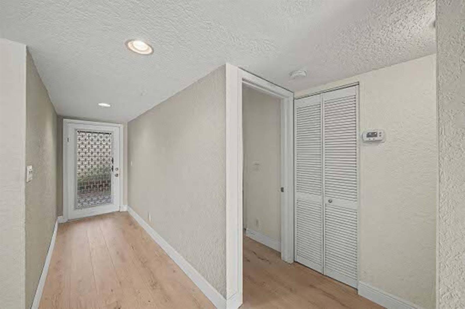 An open door reveals a bright interior with light wood flooring and a view outside — 15075 Witney Road # 108, Delray Beach FL 33484, DELRAY BEACH, FL
