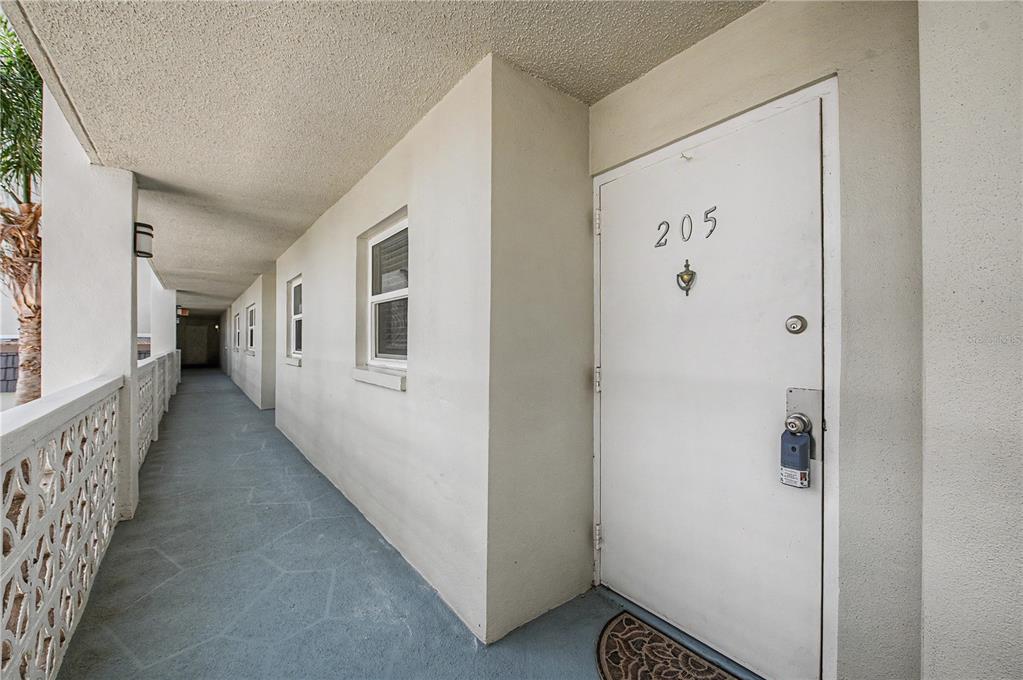 An exterior walkway leads to the entrance of unit 205 with a white door — 9 FORBES PLACE UNIT 205, DUNEDIN, FL