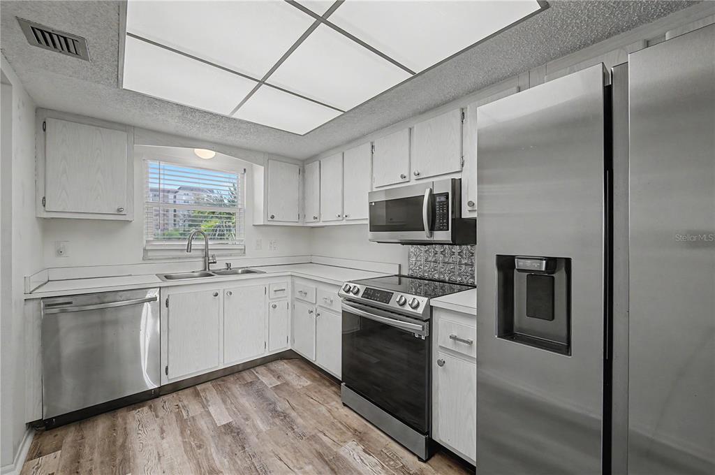 A kitchen features white cabinets, stainless steel appliances, a window, and wood-look flooring — 9 FORBES PLACE UNIT 205, DUNEDIN, FL