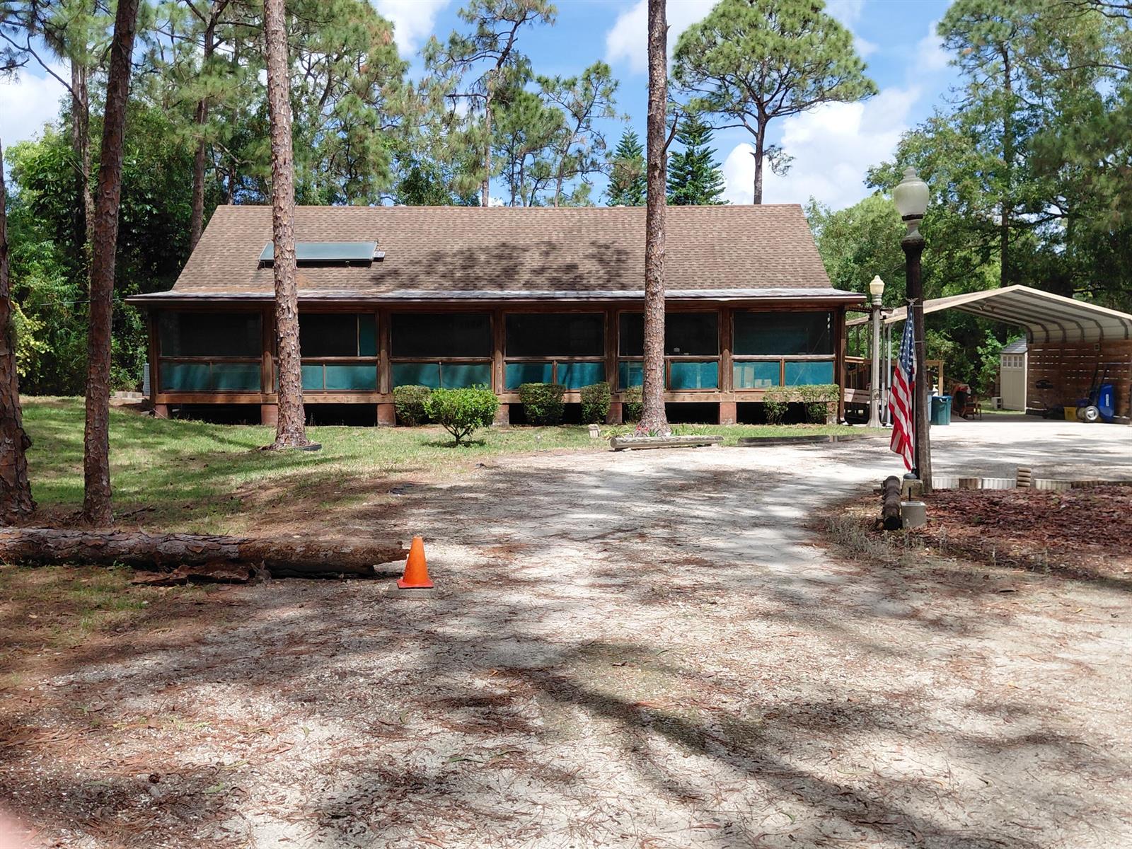 A single-story house with a screened-in porch, brown shingled roof, and a gravel driveway — 11615 Sunset Boulevard, FL 33411, FL