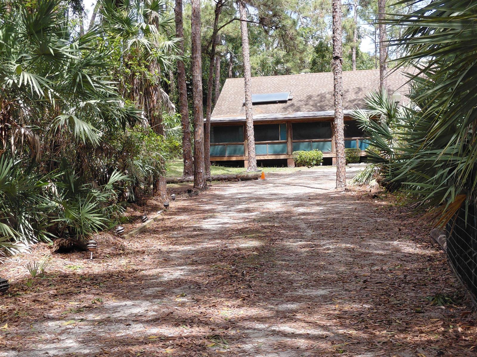 A gravel driveway leads toward a house with a screened porch and a solar panel — 11615 Sunset Boulevard, FL 33411, FL
