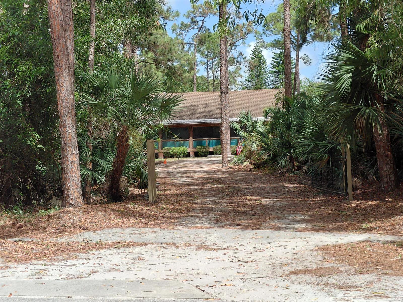 A long, leaf-covered driveway leads to a single-story house surrounded by trees and palms — 11615 Sunset Boulevard, FL 33411, FL