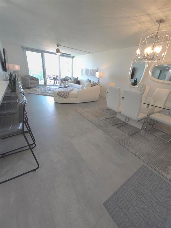 An open-concept living and dining area features large floor tiles, white furniture, and a balcony — 675 S GULFVIEW BOULEVARD UNIT 505, CLEARWATER BEACH, FL