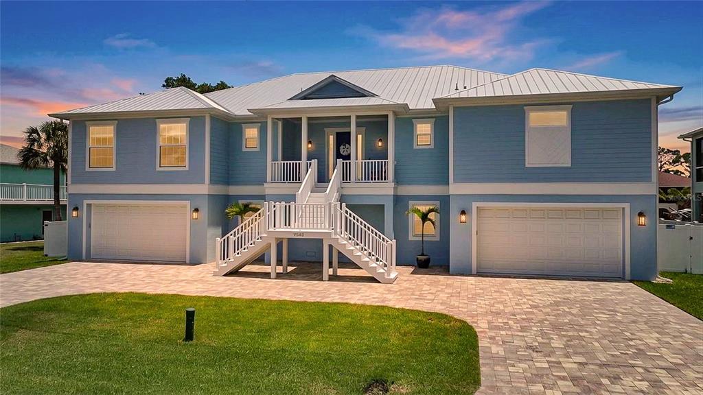 A light blue, two-story elevated house features a central staircase leading to a covered porch — 9240 PINE COVE DRIVE, ENGLEWOOD, FL