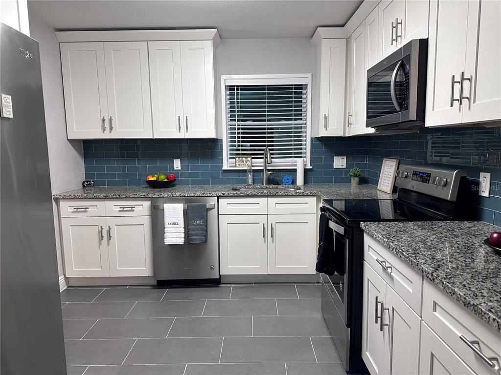 A kitchen with white cabinets, blue subway tile backsplash, granite countertops, and stainless steel appliances — 5340 5TH AVENUE S, ST PETERSBURG, FL