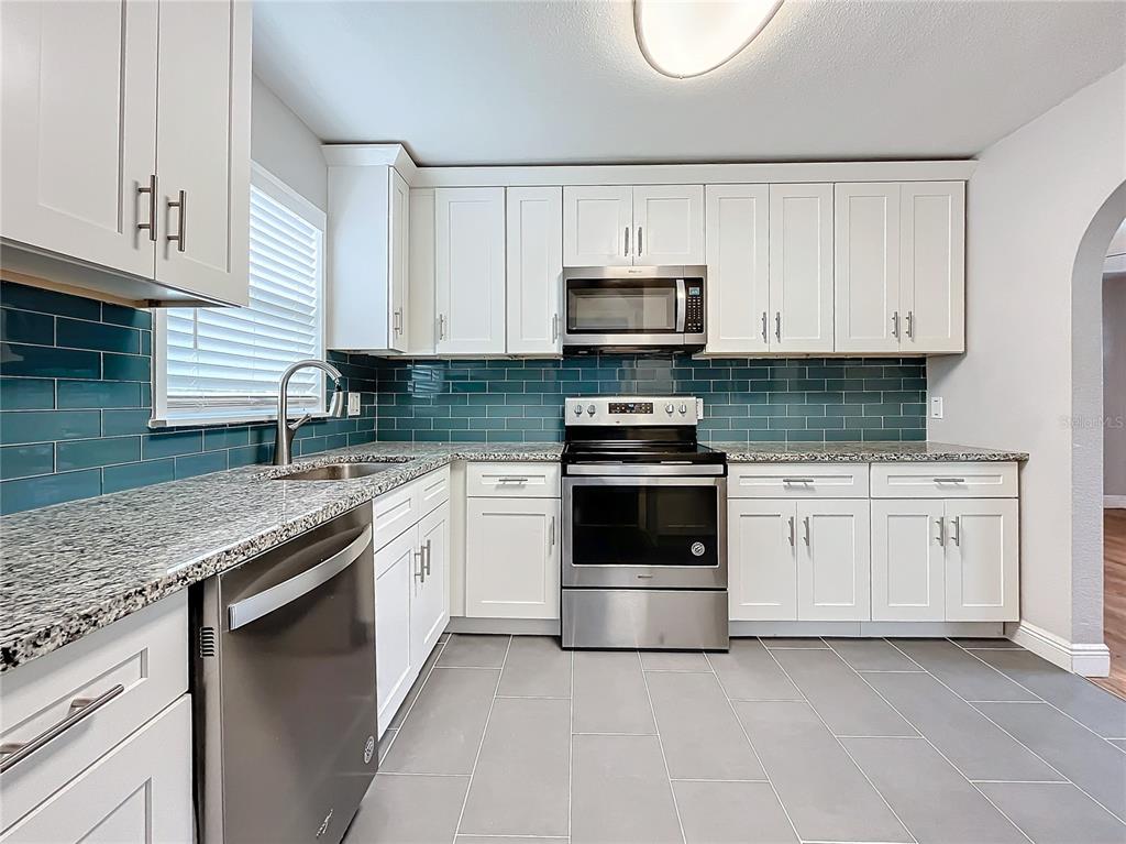 A kitchen features white cabinets, stainless steel appliances, granite countertops, and a teal subway tile backsplash — 5340 5TH AVENUE S, ST PETERSBURG, FL
