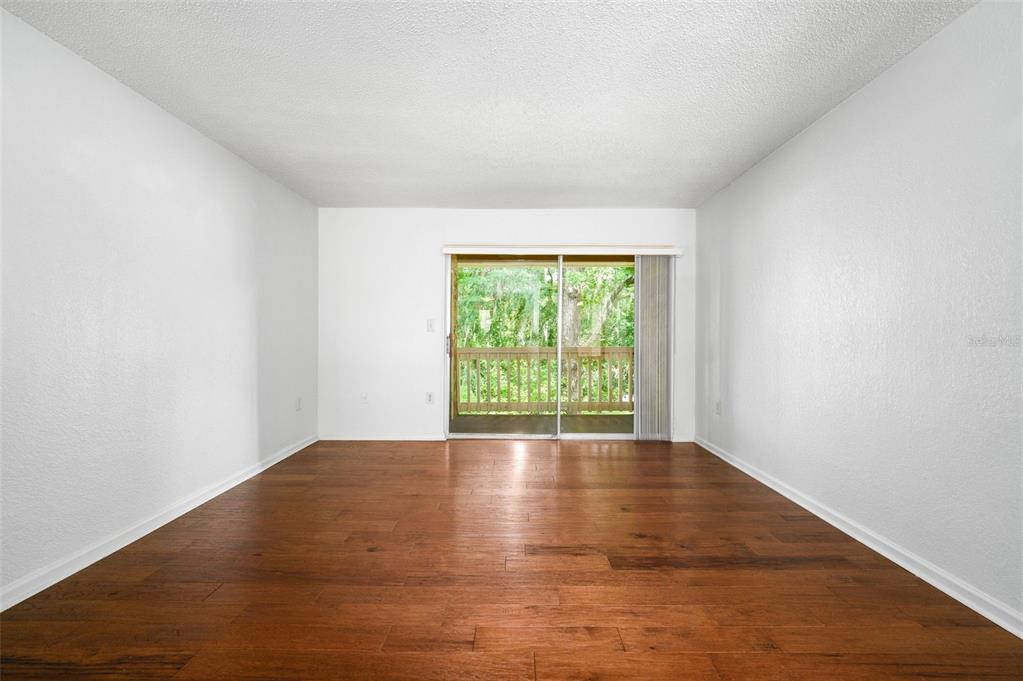 An empty room with wood-look flooring and a sliding glass door leading to a balcony — 1810 NW 23RD BOULEVARD UNIT 151, GAINESVILLE, FL