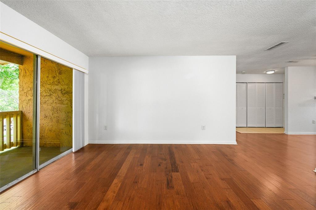A living room with hardwood floors, a large white wall, and a sliding glass door — 1810 NW 23RD BOULEVARD UNIT 151, GAINESVILLE, FL