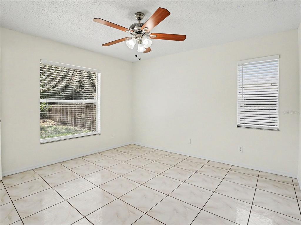 An empty bedroom features white walls, light-colored tile flooring, two windows, and a ceiling fan — 9910 N DEAN OAKS COURT, ORLANDO, FL