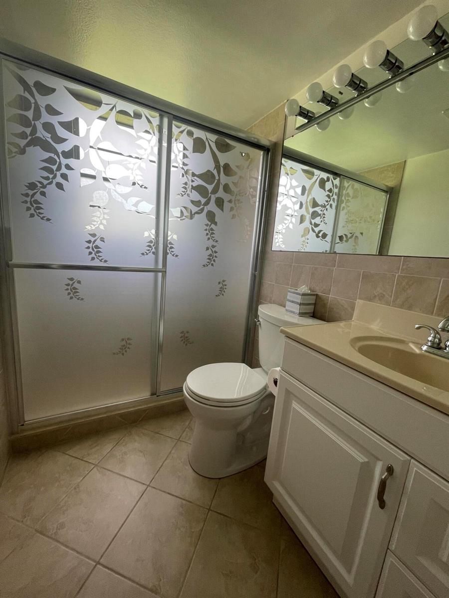 A bathroom features a vanity, toilet, and a sliding glass shower door with leaf patterns — 40 Keswick # 40, Deerfield Beach FL 33442, DEERFIELD BEACH, FL