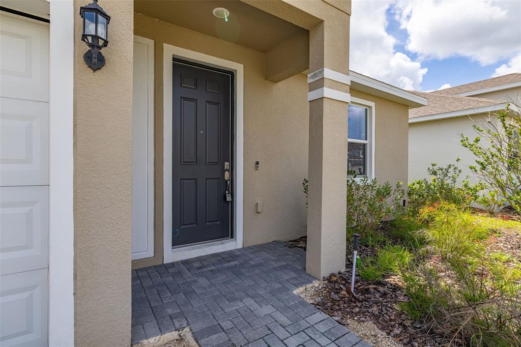 A dark gray front door is set within a tan stucco entryway with paver flooring — 1245 TUPELO TRAIL, HAINES CITY, FL