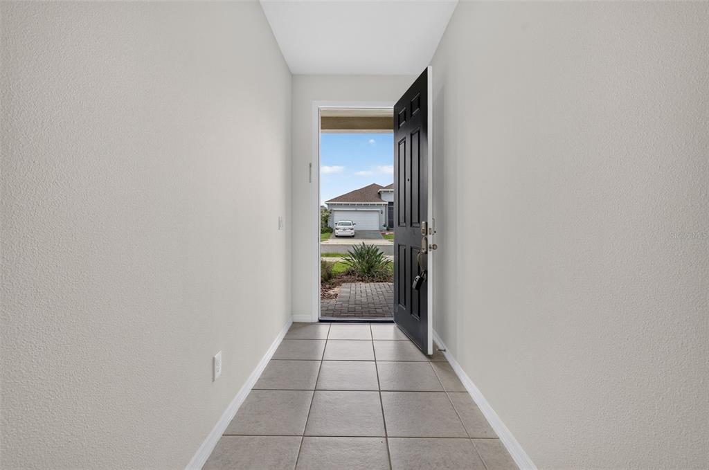 An entryway with light-colored walls and tiled flooring leads to an open front door — 1245 TUPELO TRAIL, HAINES CITY, FL