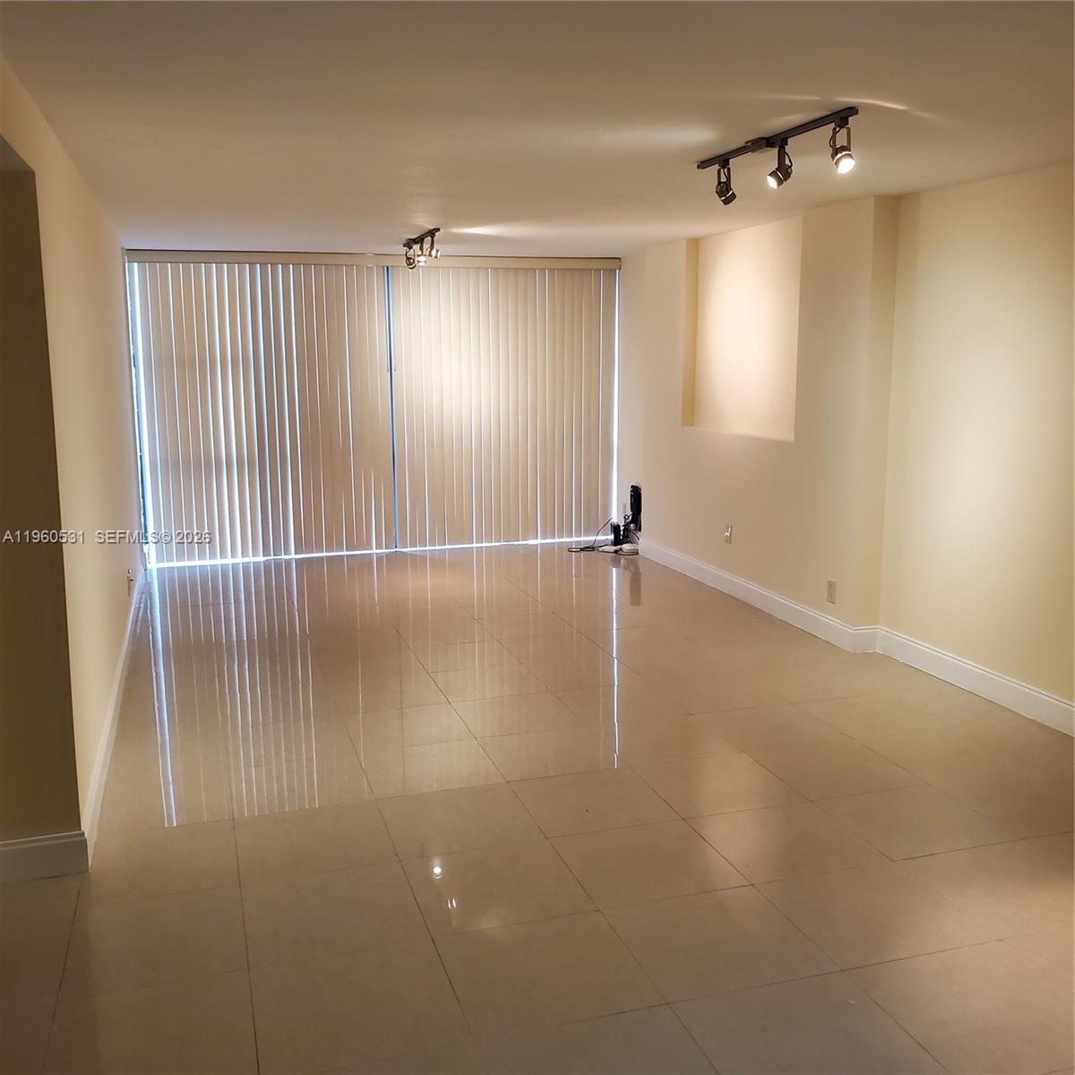An empty room features light-colored tile flooring, cream walls, and floor-to-ceiling vertical blinds — 800 Parkview Dr # 416, Hallandale Beach FL 33009, HALLANDALE BEACH, FL