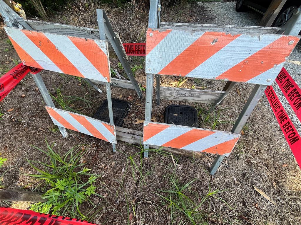 Two orange and white construction barricades surround two utility access covers on a grassy area — 306 NW 12TH AVE, GAINESVILLE, FL