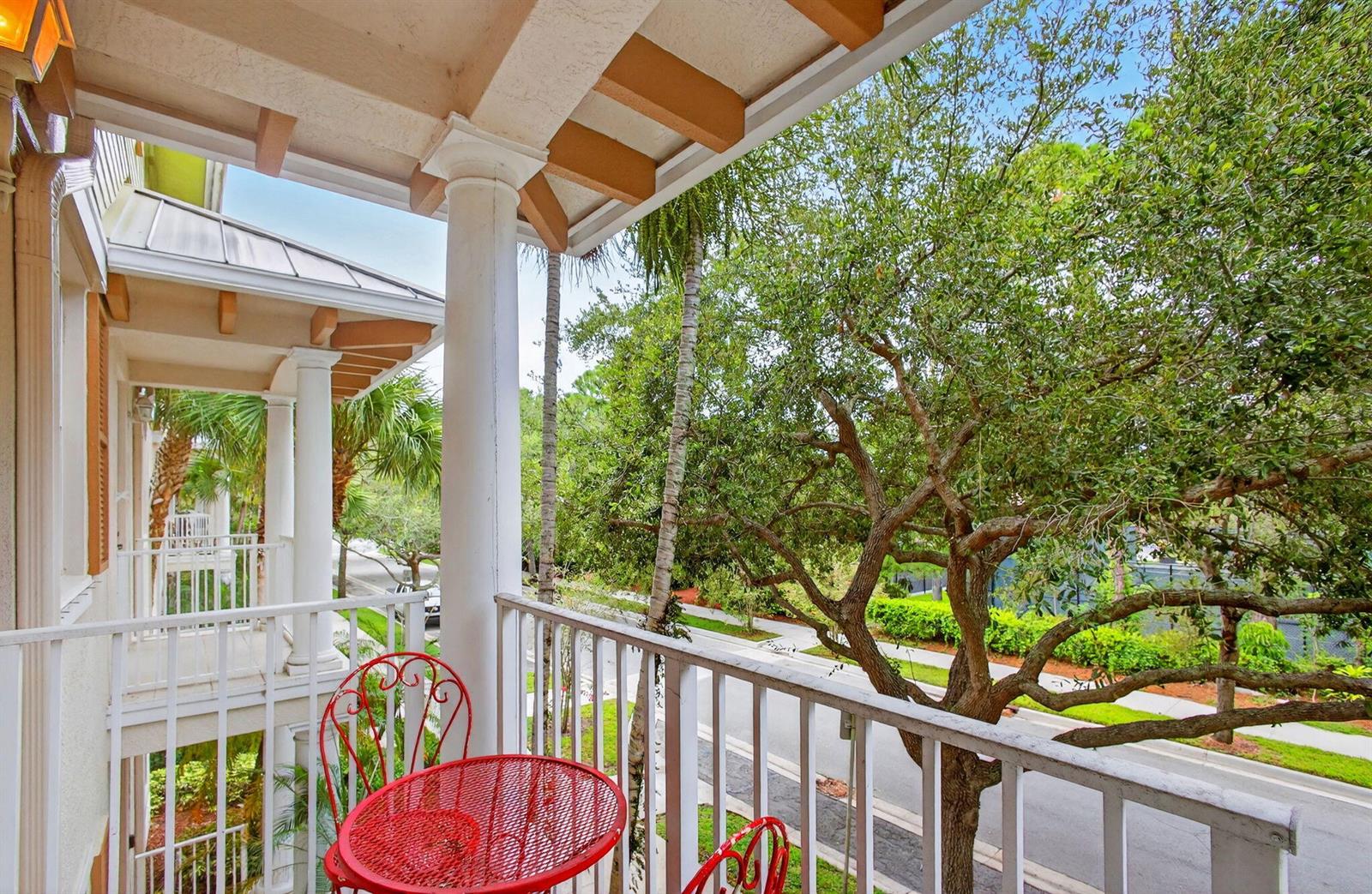 A covered balcony with white railings, a red bistro set, and views of a street — 1562 Grande Cull Way, Jupiter FL 33458, JUPITER, FL