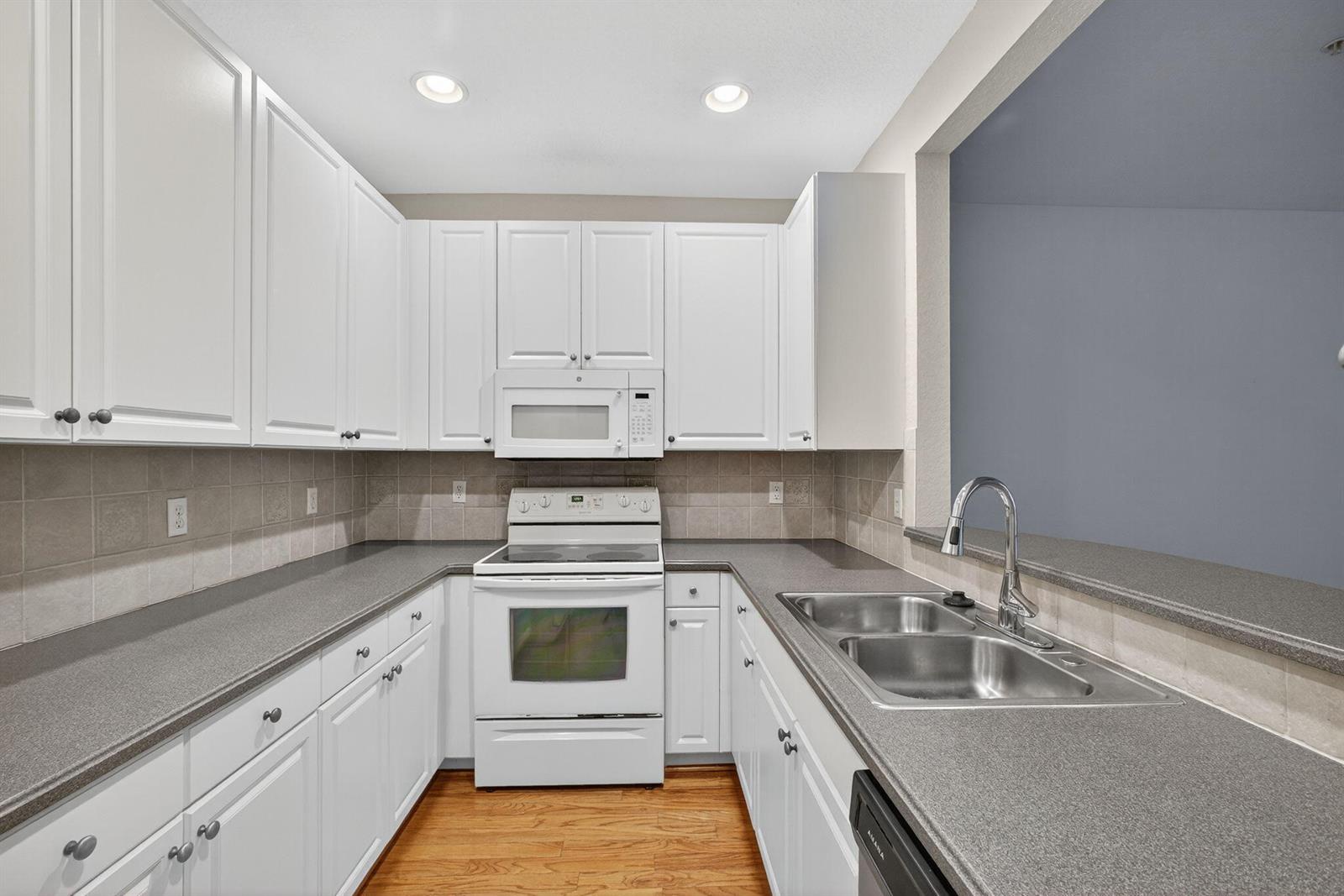 A kitchen with white cabinets, gray countertops, stainless steel sink, and white appliances — 1562 Grande Cull Way, Jupiter FL 33458, JUPITER, FL