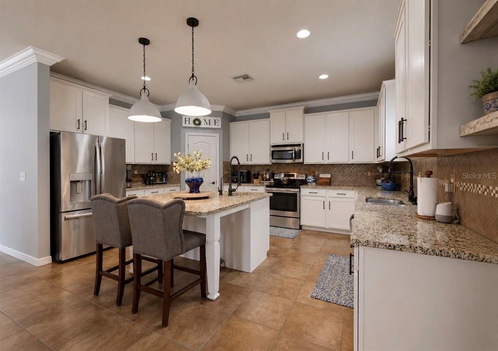 A kitchen features white cabinets, granite countertops, a central island, and stainless steel appliances — 12426 FAIRLAWN DRIVE, RIVERVIEW, FL