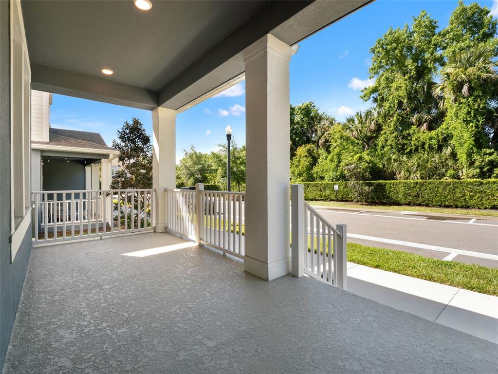A covered porch features white railings, concrete flooring, and views of a street and trees — 1128 SPOTTED SANDPIPER LOOP, WINTER SPRINGS, FL