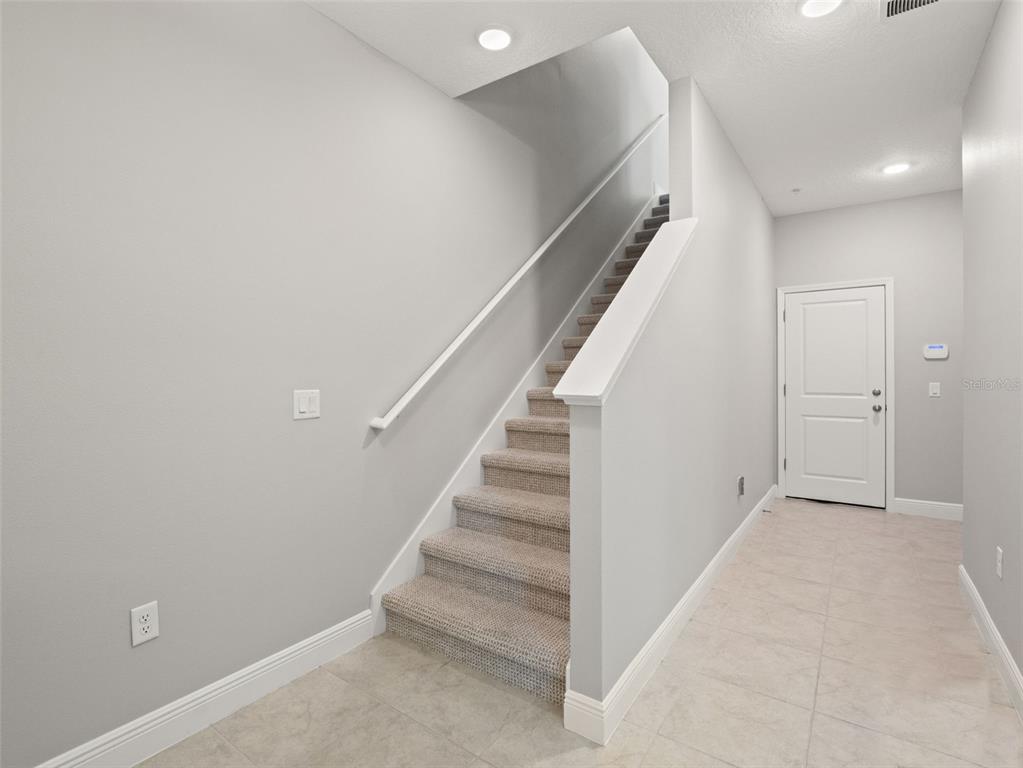 A carpeted staircase with a white railing sits in a foyer with light-colored tile flooring — 1128 SPOTTED SANDPIPER LOOP, WINTER SPRINGS, FL