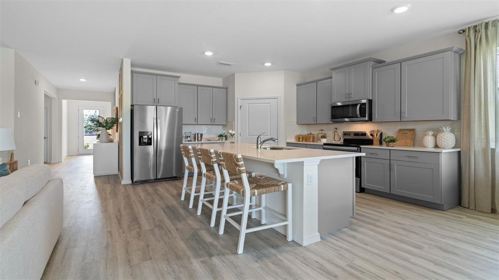 A kitchen features gray cabinets, a white island with bar stools, and light wood flooring — 3032 KINGSMAN TRAIL, ORMOND BEACH, FL