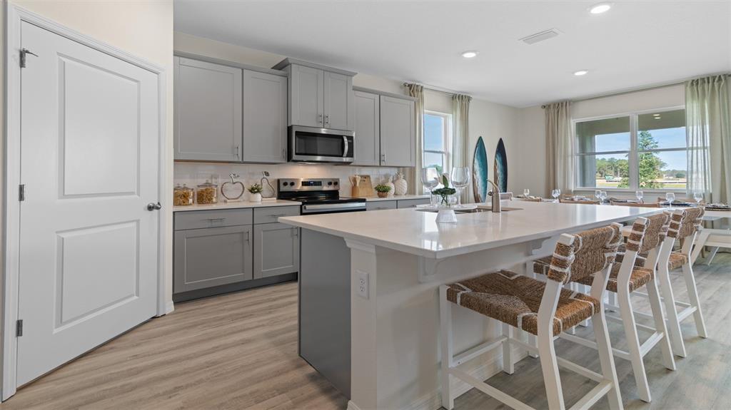 A kitchen features gray cabinets, a large white island with bar stools, and light flooring — 3032 KINGSMAN TRAIL, ORMOND BEACH, FL