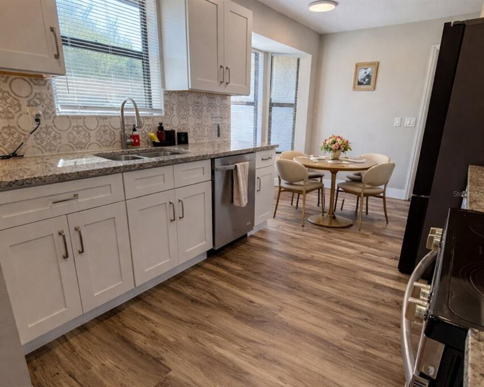 A kitchen features white cabinets, granite countertops, a patterned backsplash, and a small dining area — 1413 SANDALWOOD DRIVE, PLANT CITY, FL