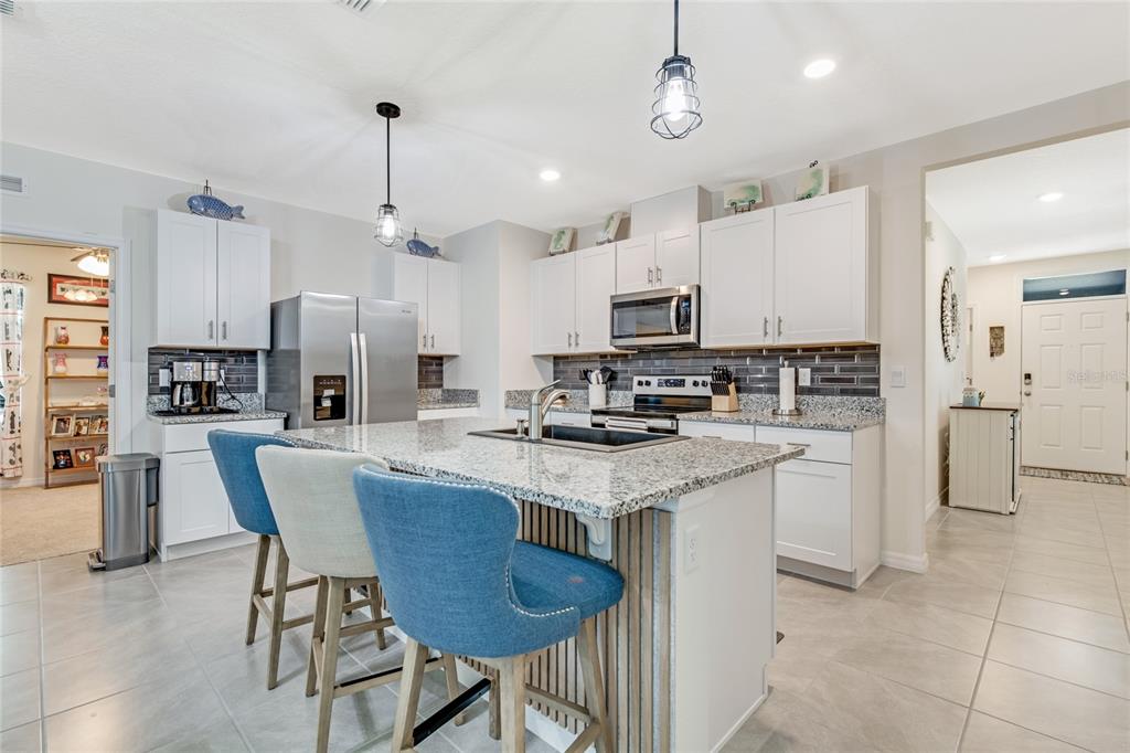 A kitchen features white cabinets, granite countertops, a central island with blue chairs, and stainless appliances — 1362 CORK DRIVE, ORMOND BEACH, FL